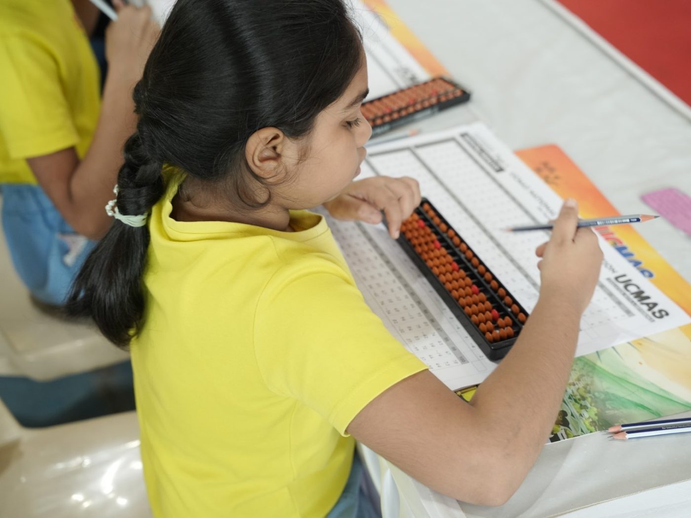 A UCMAS student working through a problem sheet with her abacus